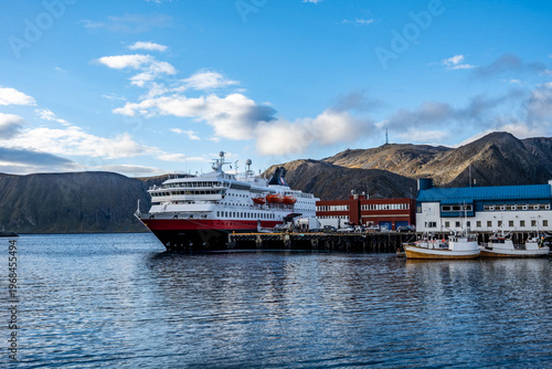 Large cruise ship and expedition vessel docked in the harbor of Honningsvag near North Cape, Norway, under a blue sky