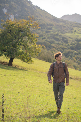  Young man hiking on a green mountain slope in Asturias, Spain, at sunny autumn day
