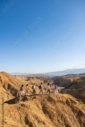 Group Of Friends Hiking In Single File Along Rugged Desert Ridge Under Clear Blue Sky
