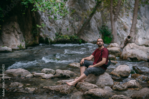 Tableau sur toile A young male tourist near a clear mountain stream in the rocks overgrown with gr
