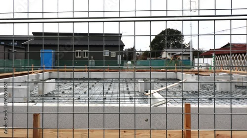 Slow horizontal pan of newly completed residential house foundation construction site with reinforced concrete base and rebar grid behind fence