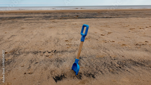 A toy plastic and wood spade standing up on a sandy beach
