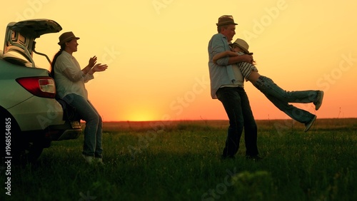 Fotografi Father child playing around car, mother happy, picnic in nature, sunset