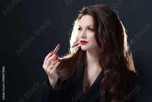 Luxurious brunette applying red lipstick, dark studio