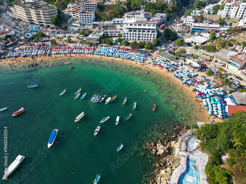 Fotografie Vibrant Caleta Beach in Acapulco, Mexico, crowded with people enjoying the sunny day, seen from an aerial drone perspective with many boats in the bay