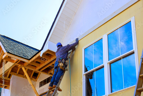 Worker is using ladder to place siding on new building at construction site.