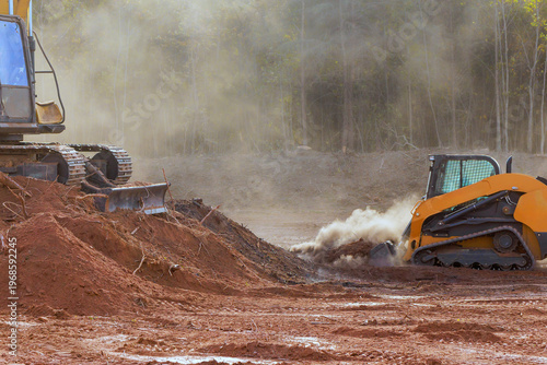 Heavy machinery clears land in construction zone as dust dirt fill air in forest setting.