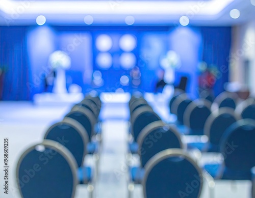 Blurred Conference Room Setup with Blue Chairs and Stage.