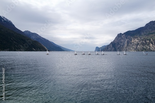 Line of small sailboats training on Lake Garda under cloudy sky