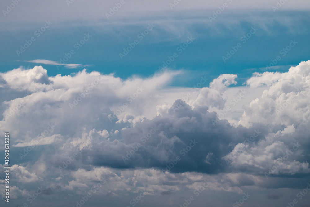 Obraz premium a multi-layered sky featuring a dense wall of dark grey and white cumulus clouds at the bottom, set against a bright blue sky with soft, wispy cirrus cloud formations