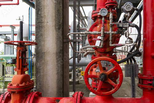Red pipes form industrial valve system. Metal fittings connect robust, rusted machinery. Handwheels and gauges dominate foreground. Structure suggests high-pressure fluid handling