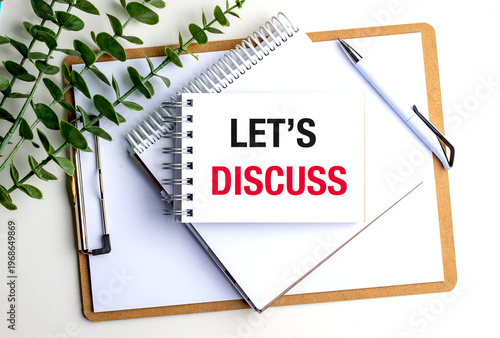 Notebook with lets discuss text with green leaves and pen on desk communication meeting planning concept