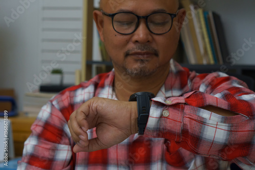 Businessman checking time and looking at smart wrist watch at home office.  Asian man seeing clock to work. Desk with laptop, annual, and summary report.Time out for appointment meeting