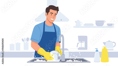 Happy young man wearing a blue apron and yellow gloves washes dishes in a modern kitchen with clean white cabinets and appliances.