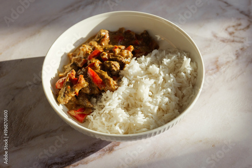 Savory beef curry with red bell peppers and white rice served in a bowl on a marble countertop