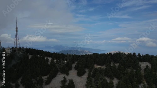 A tall tower stands on a forested mountain overlooking islands in the distance under a cloudy sky.
