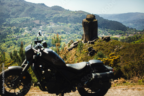Mountain landscape in Peneda Geres with granite rock formation and green valley, with blurred motorcycle in foreground suggesting travel and road trip.