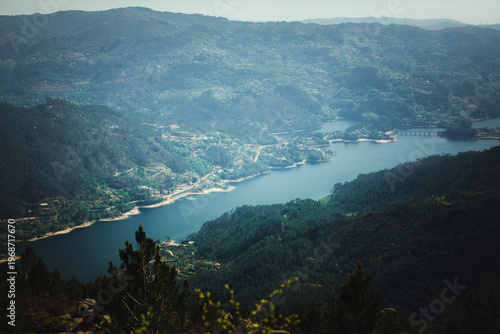 Panoramic view of Cavado river in Peneda Geres with forested hills, villages, and a bridge crossing the water under soft haze.
