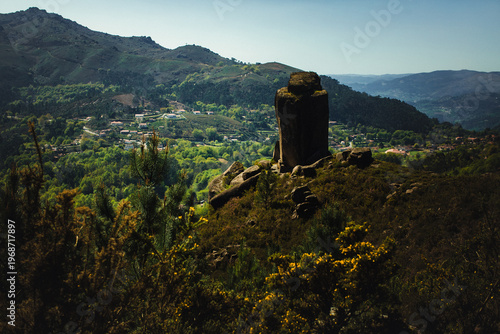 Granite rock formation on a hill in Peneda Geres overlooking a green valley with villages and mountains in the background.