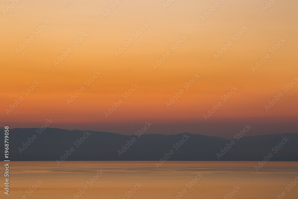 Obraz premium The sun rises over the mountains on the Greek mainland and reflects in the Ionian Sea on a beautiful cloudless morning taken from the island of Corfu