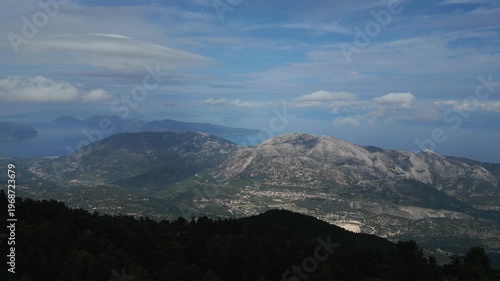 Expansive mountain landscape meets the sea under a cloudy blue sky.