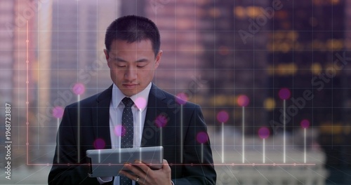 Holding tablet, mid-adult Asian executive in dark suit dotted tie analyzing digital overlay on roof