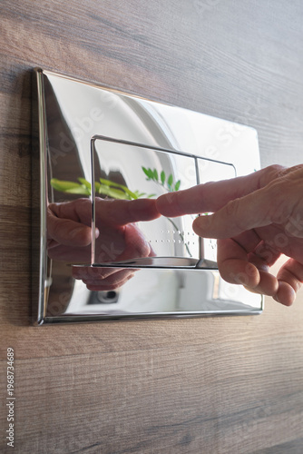 Male hand pressing button on modern toilet flush panel. Flush button on a toilet. Toilet flush press with two separate buttons from chrome on a wall. 