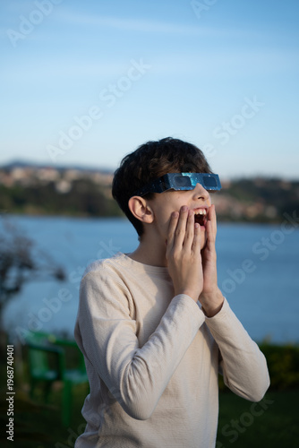 Teenage boy observing solar eclipse with protective glasses outdoors, vertical image

