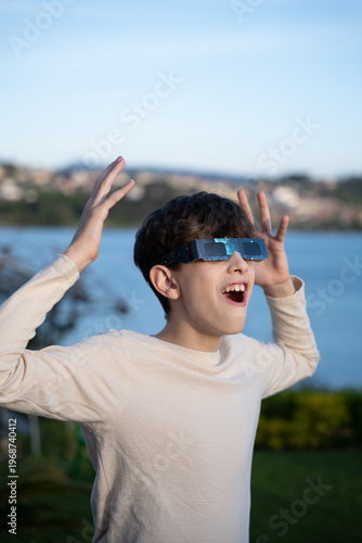 Teenage boy observing solar eclipse with protective glasses outdoors, vertical image

