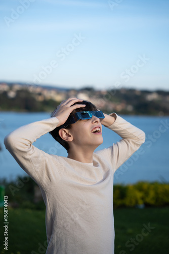 Teenage boy observing solar eclipse with protective glasses outdoors, vertical image

