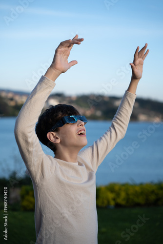Teenage boy observing solar eclipse with protective glasses outdoors, vertical image

