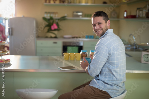 Mint green kitchen counter is basking in warm light with blue mug, tablet, pastries