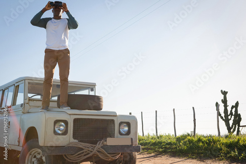 Vintage off-road vehicle is sitting on dirt track beside grassy field, spare tire and rope