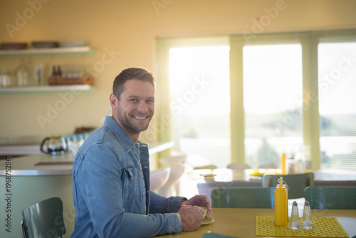 Yellow table with mustard and shakers is sitting near green chairs by sunlit window blinds