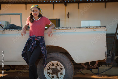 Worn white pickup truck is resting on dirt, rusted bed holding black bag and white cooler