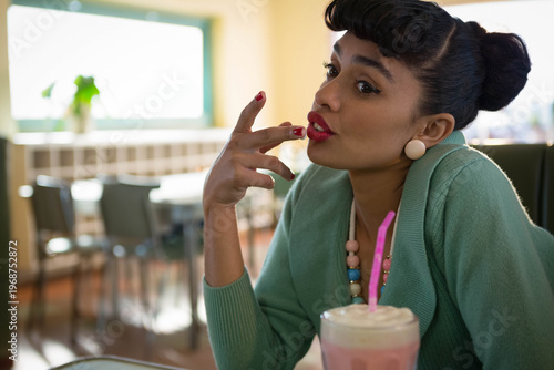 Milkshake with whipped cream and pink straw sitting on table near bright window and plant