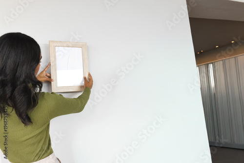 Woman seeing blank wall placing wood frame, aligning with animated guide for interior design