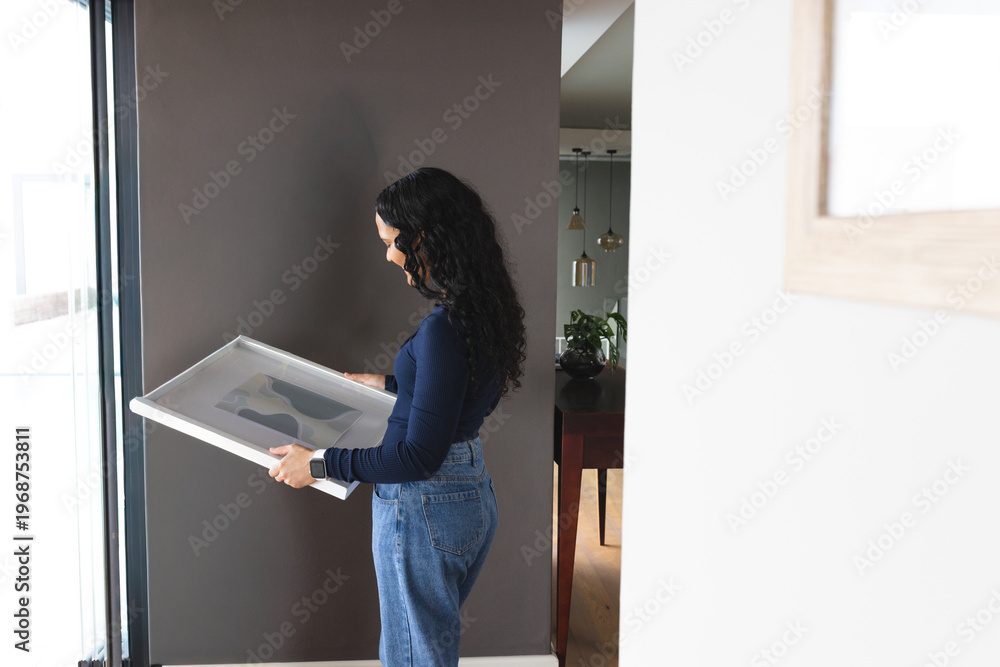 Fototapeta premium Framed artwork is leaning near tall glass door against dark gray wall, wooden table visible