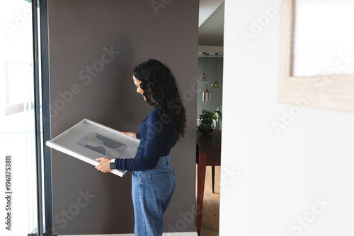 Framed artwork is leaning near tall glass door against dark gray wall, wooden table visible