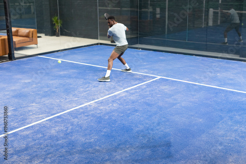 Fotografia Man preparing backhand return on sports court, incoming yellow ball causing anim