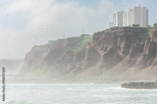 Misty Coastal Cliffs and Ocean Waves Below Residential High-Rises on a Foggy Morning. Lima City, Peru