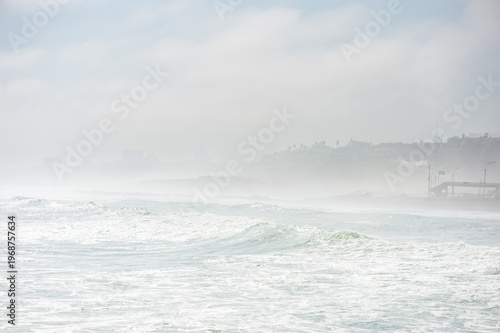Foggy Coastal Ocean Waves With Misty Shoreline and Distant City Silhouette at Morning in Lima City, Peru
