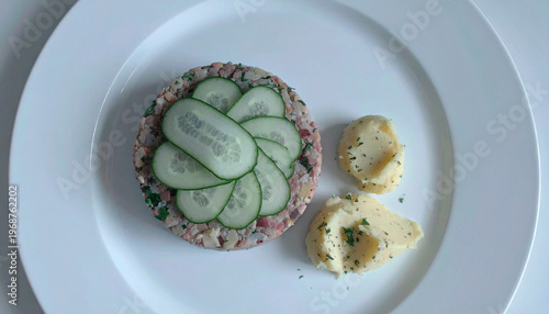 Meat tartare topped with fresh cucumber slices served with herb mashed potatoes on white plate