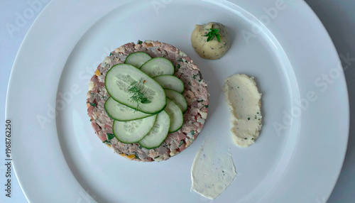 Meat tartare topped with fresh cucumber slices served with herb mashed potatoes on white plate