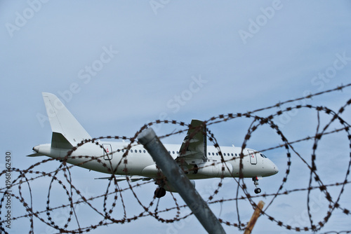 Tableau sur toile Jet Landing: White Plane, Barbed Wire and Cloudy Sky