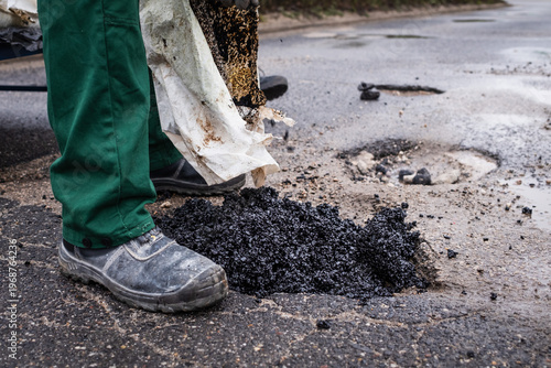 Tableau sur toile Road workers repair a pothole on a street by pouring asphalt from a bag
