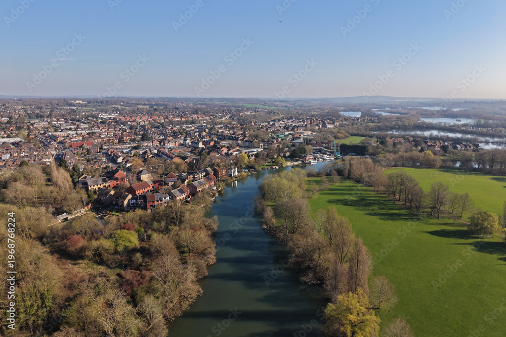 Fototapeta premium Aerial drone view of Reading in Berkshire, England, featuring the River Thames flowing through the town with surrounding urban landscape, bridges, and green spaces.
