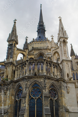 Gothic spires rise above ornate arches and statues against a bright sky. Stone tracery and stained glass frame the cathedral in Reims. Light and shadows reveal details across the facade.