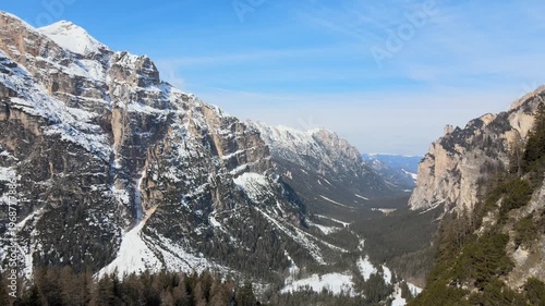 Aerial drone footage slowly pulling back over dramatic alpine valley with snow covered mountain peaks