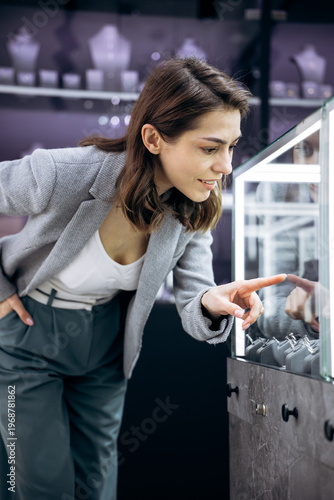Smiling woman pointing at displayed items, choosing a gift or indulging in retail therapy at a high-end jewelry store